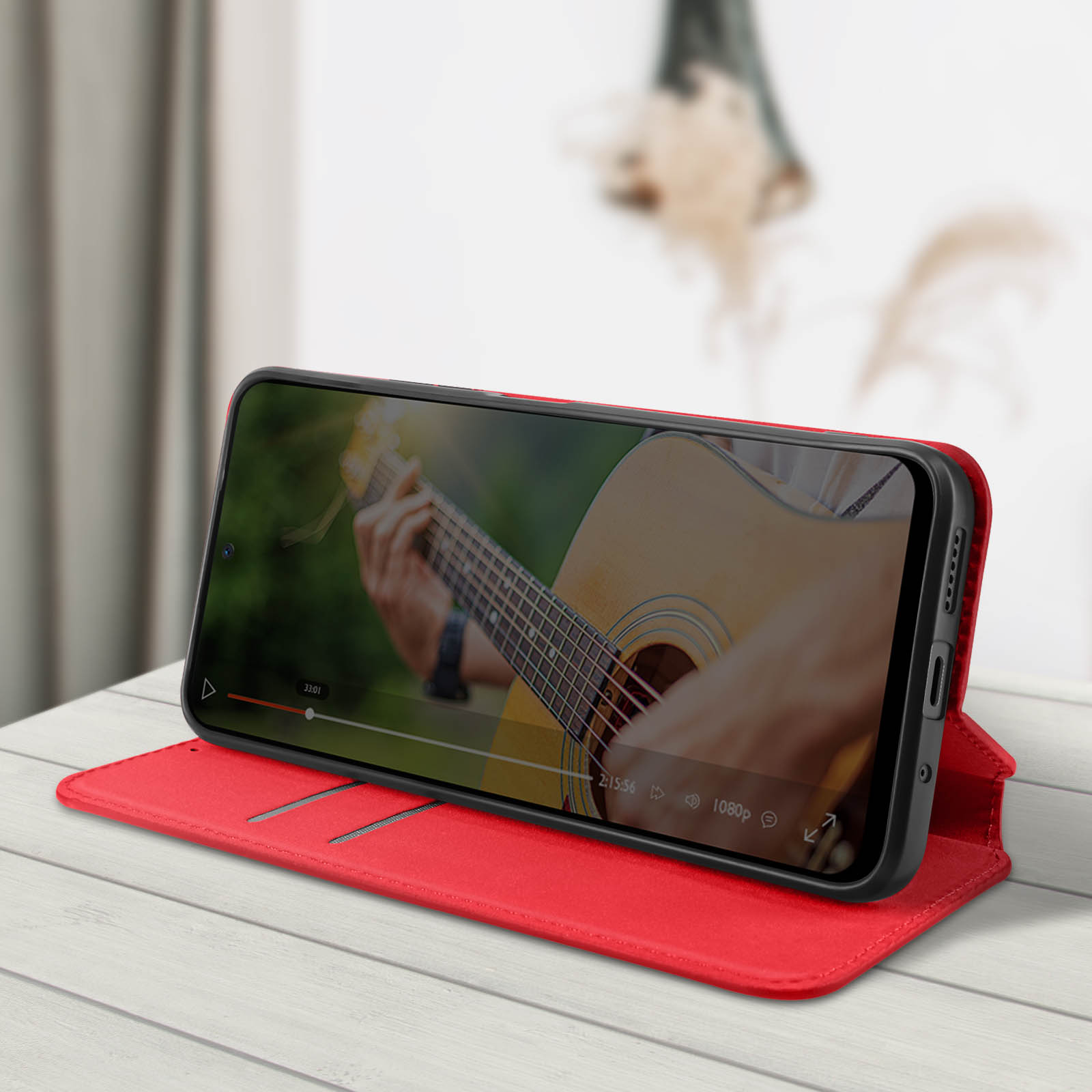 Telefono in custodia rossa, aperto ad angolo, mostra video di persona che suona la chitarra.