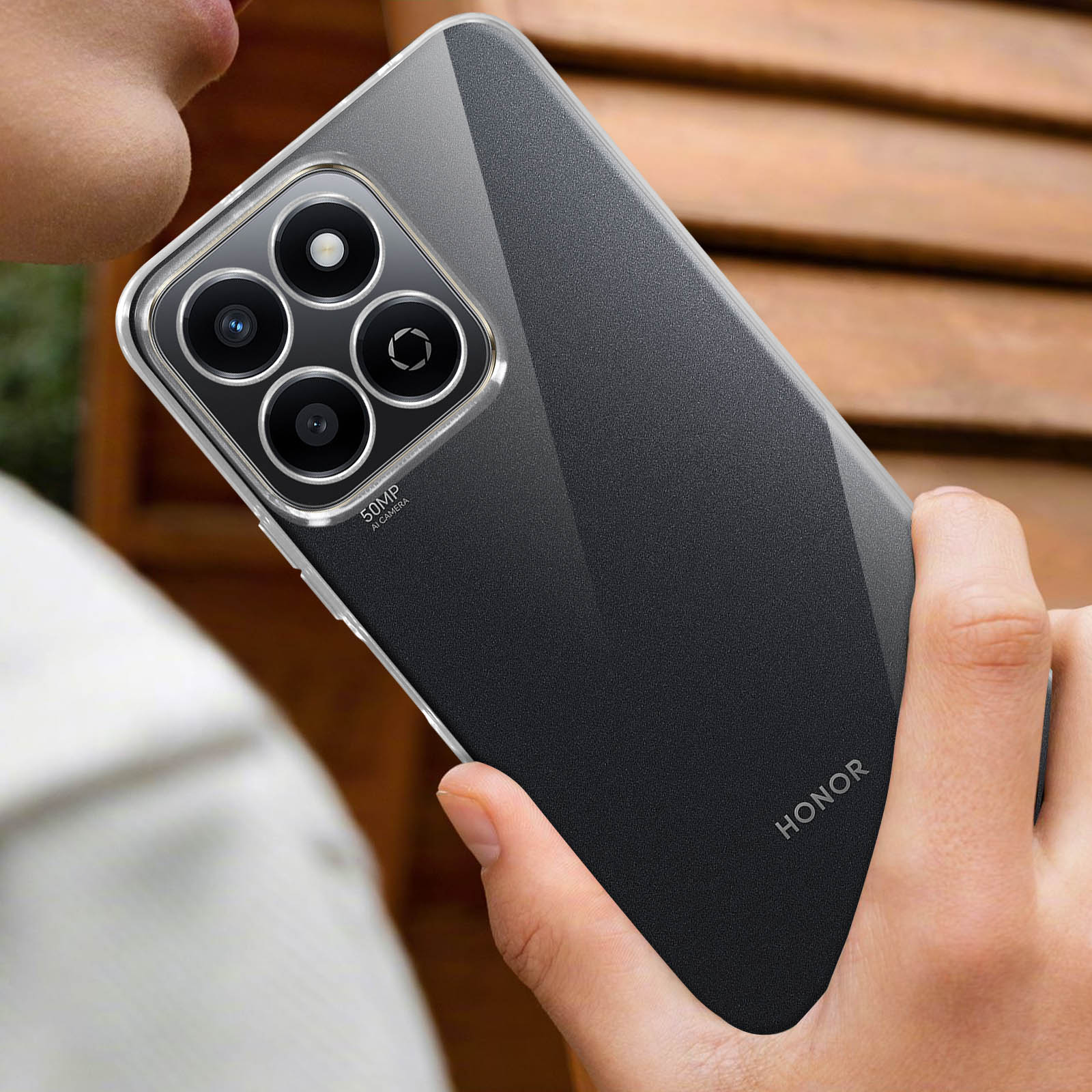 Persona che tiene in mano un telefono nero in una custodia trasparente. Il telefono ha un modulo fotocamera, marchio HONOR.