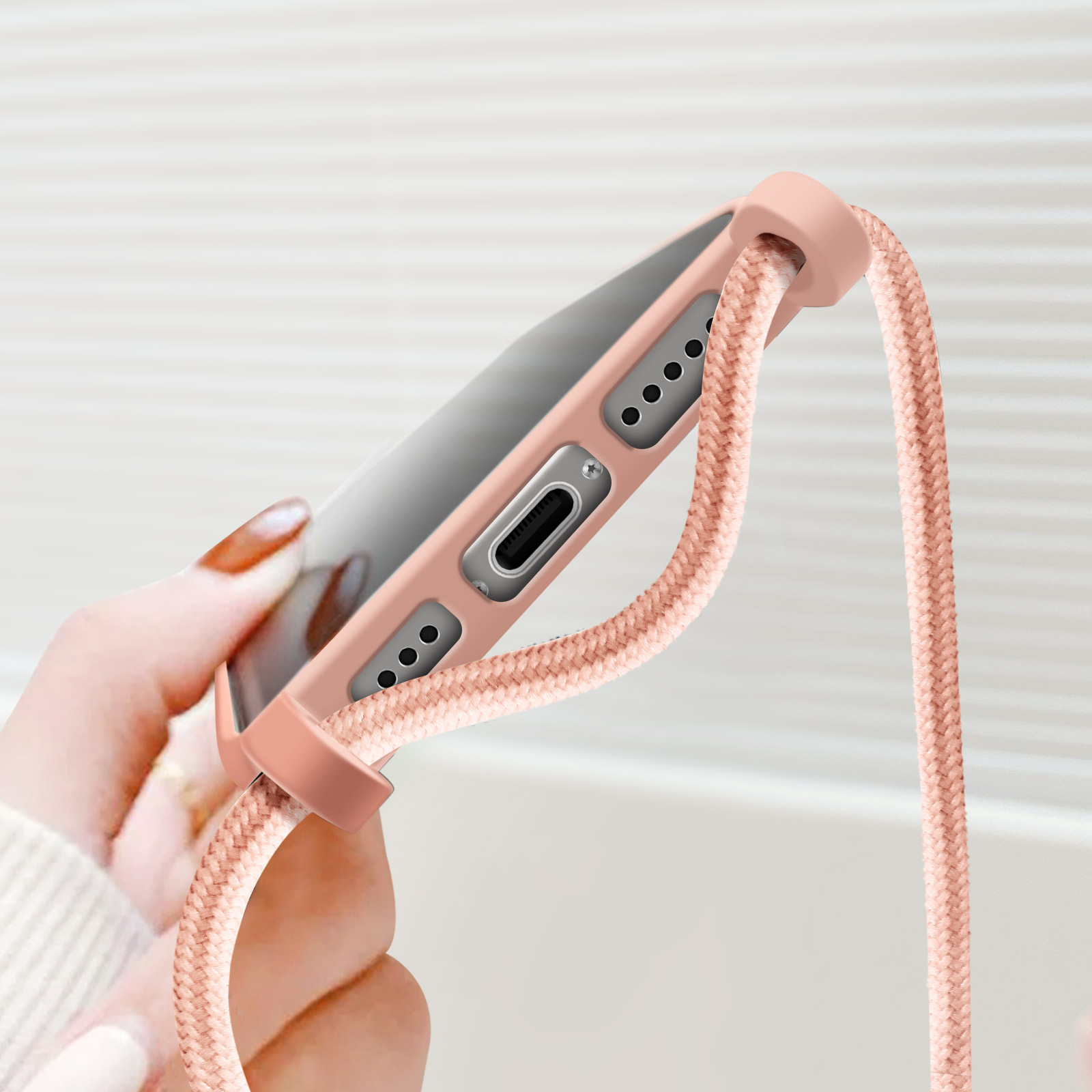 Una mano che tiene una custodia per telefono con un cordino. La custodia e il cordino sono rosa.