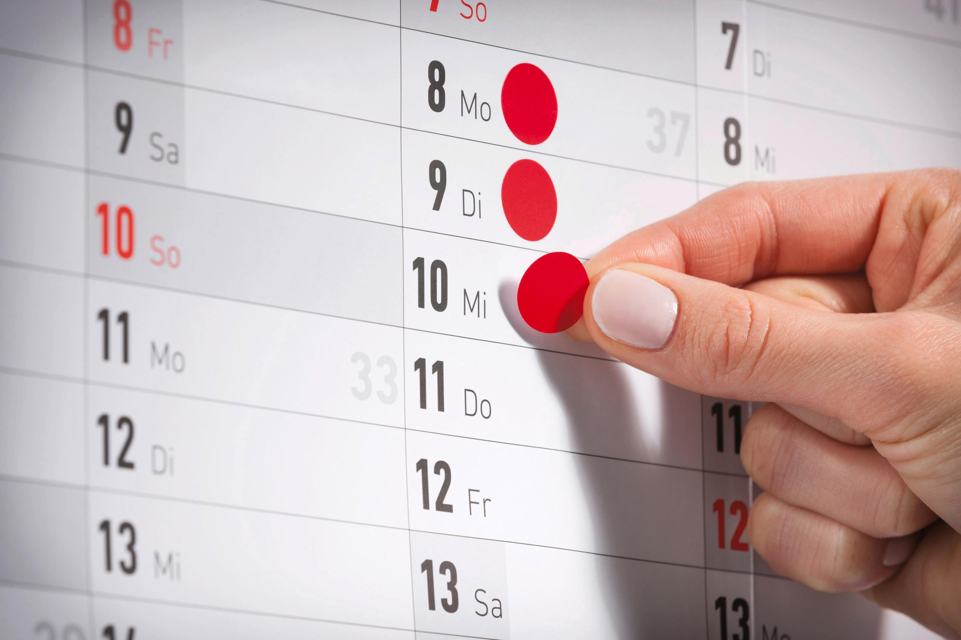 Ręka zaznacza czerwone kropki w kalendarzu. Widoczne są dni tygodnia.