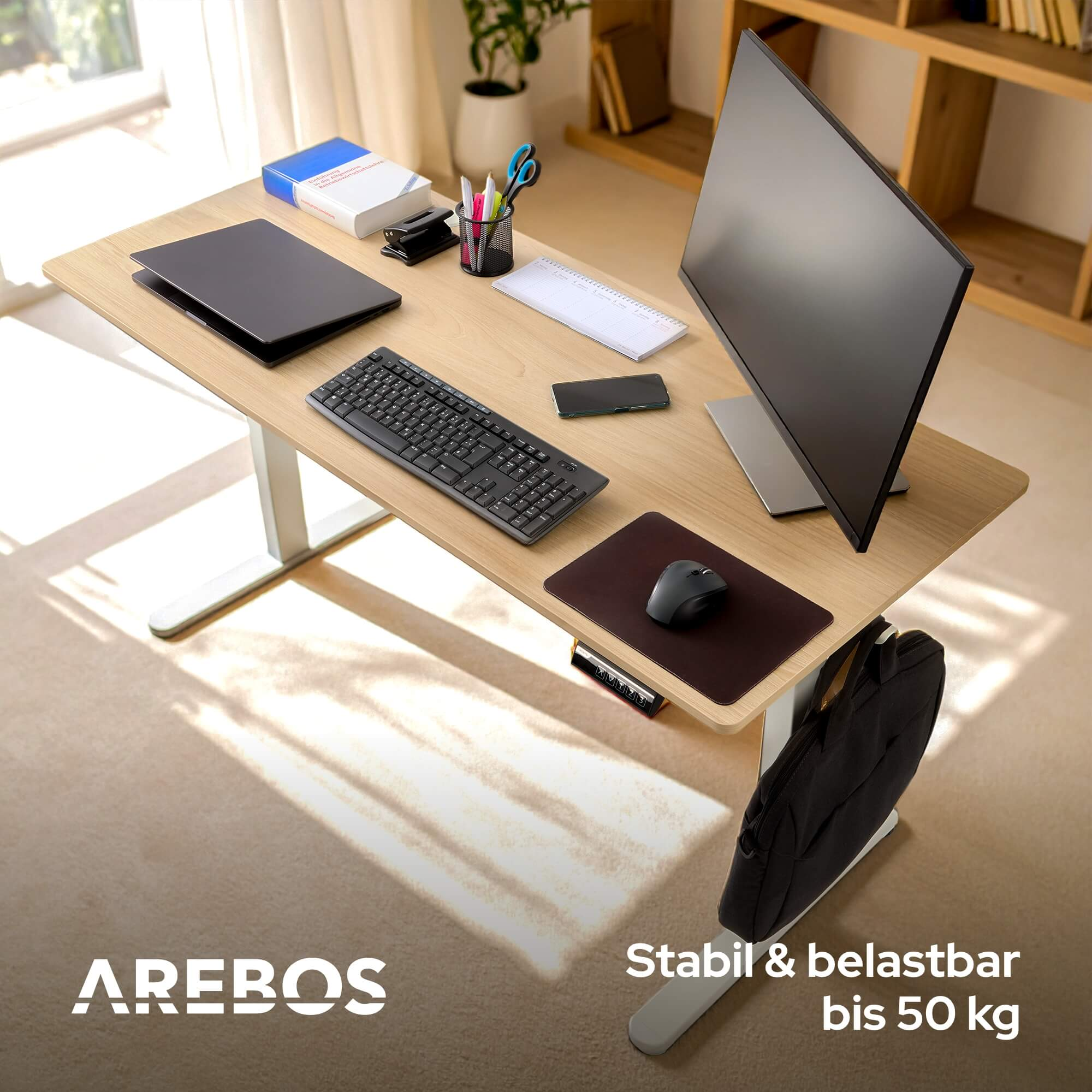 Ein Schreibtisch mit Monitor, Tastatur und Zubehör. Eine schwarze Tasche hängt. Der Schreibtisch hat eine Holzoberfläche und weiße Beine.