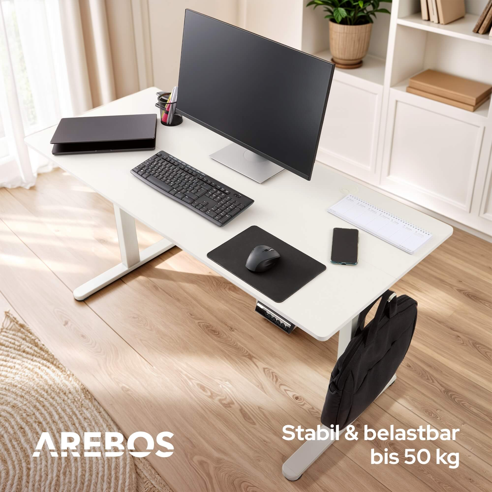 Ein weißer Schreibtisch mit Monitor, Tastatur und Zubehör. Eine Tasche hängt an der Seite.
