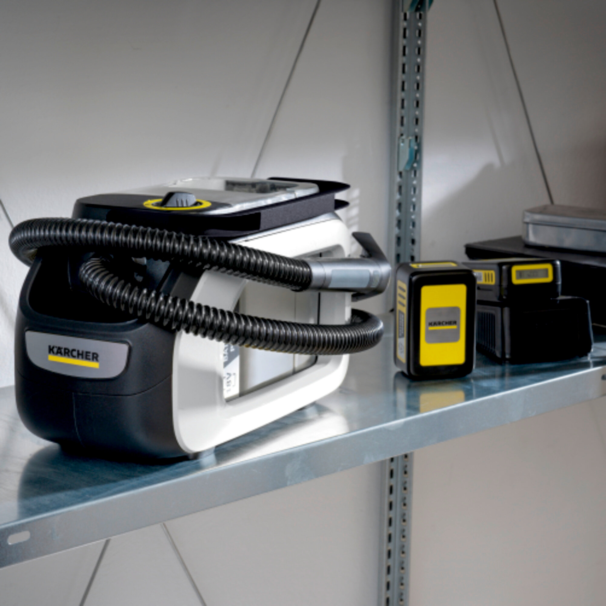 Schwarzer und weißer Kärcher Staubsauger auf einem Regal mit Batterien. Hintergrund ist eine weiße Wand.