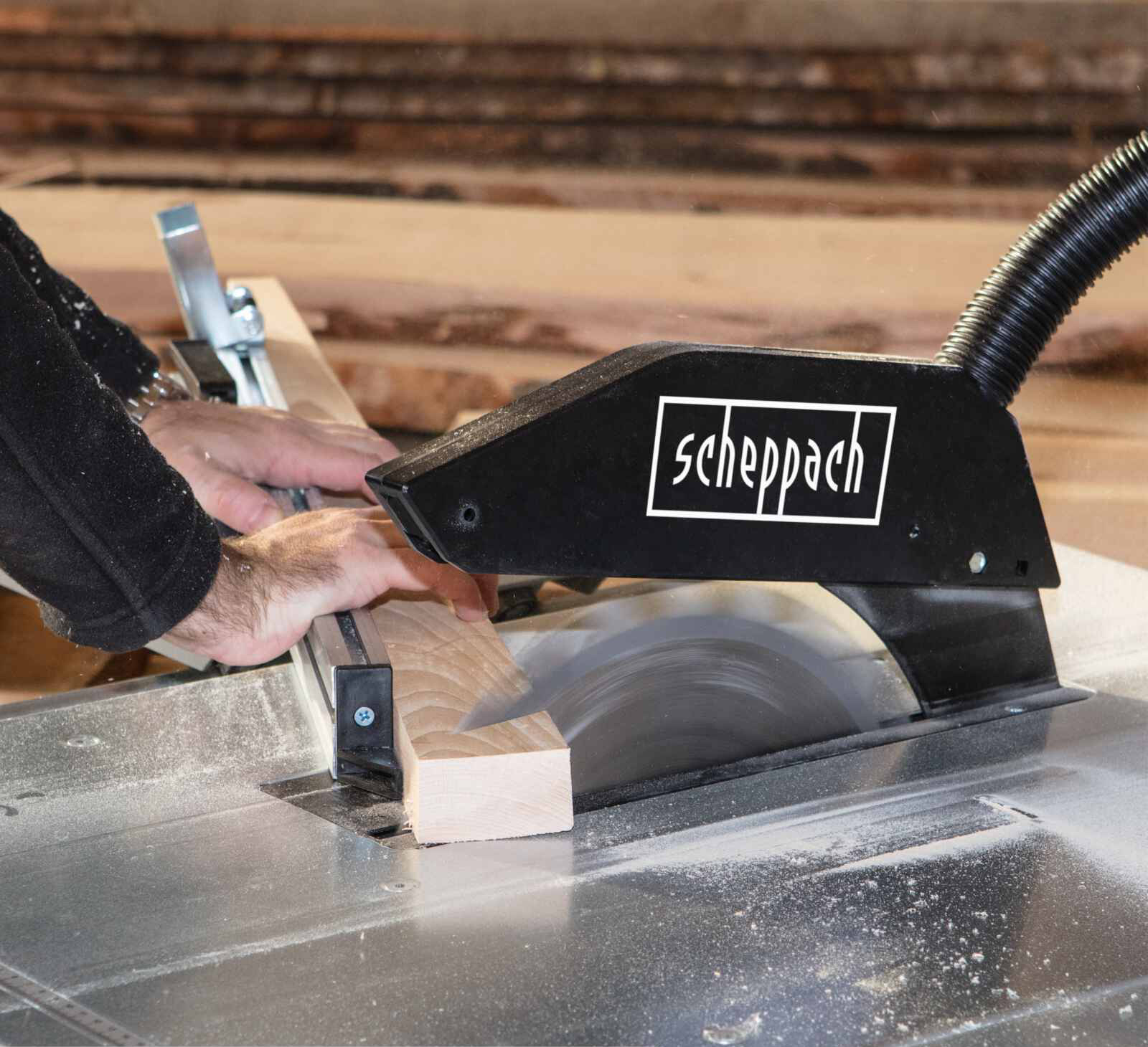 Man gebruikt tafelzaag. Zaagt een houten plank. Zwarte zaagkap. Houten achtergrond.