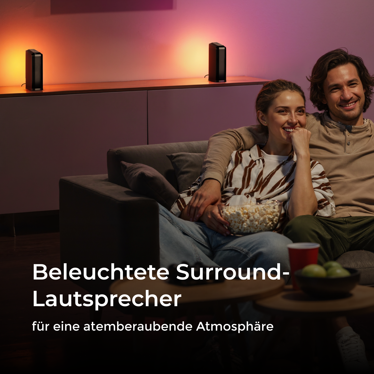 Paar auf dem Sofa, das fernsieht, mit Popcorn und Lautsprechern im Hintergrund.