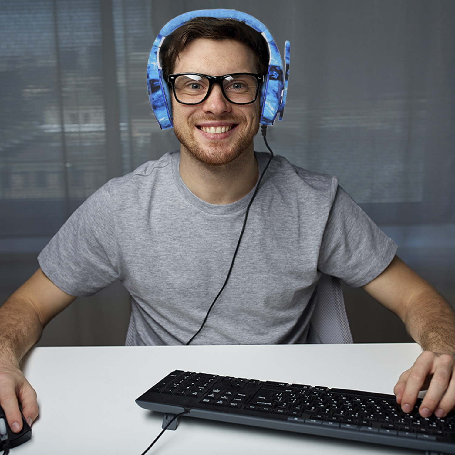 Hombre con gafas y auriculares azules, sonriendo a la cámara, sentado en un escritorio con teclado.