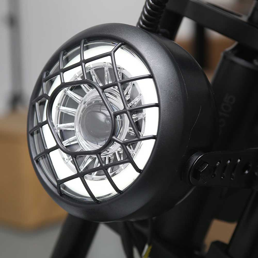 Primer plano de un faro de bicicleta negro. La luz está rodeada por una rejilla protectora de metal.