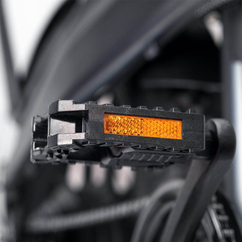 Nahaufnahme eines Fahrradpedals mit einem reflektierenden orangenen Teil. Schwarzes Pedal und Rahmen.