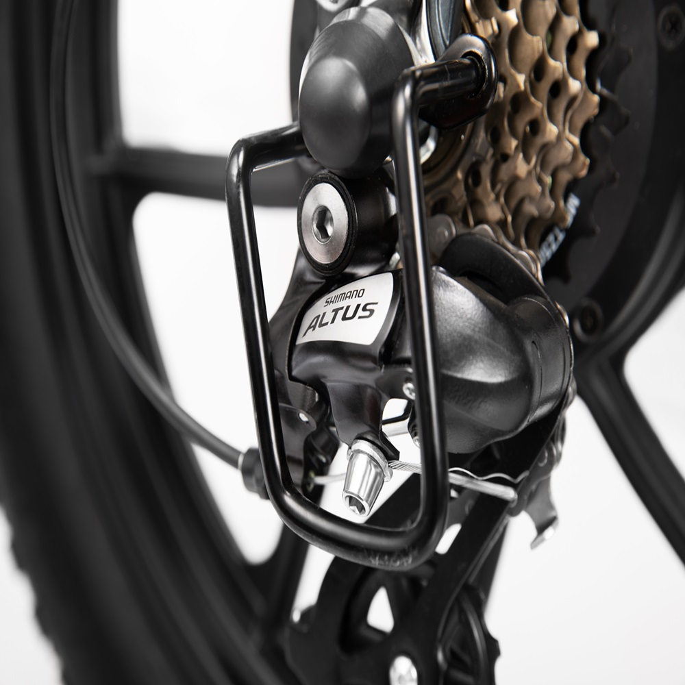 Nahaufnahme eines Shimano Altus Schaltwerks am Hinterrad eines schwarzen Elektrofahrrads, Speichen sichtbar.