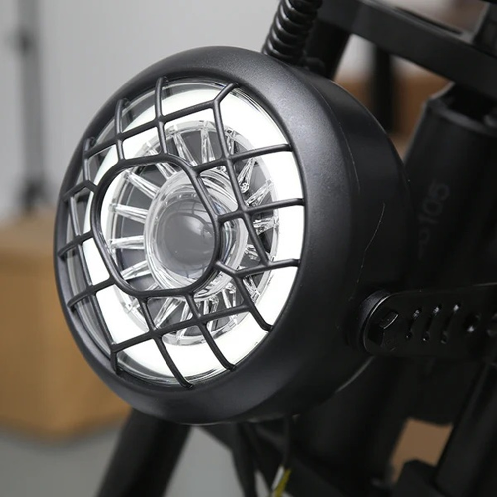 Primer plano de un faro de bicicleta eléctrica negra con una rejilla protectora. Luz blanca y brillante visible.