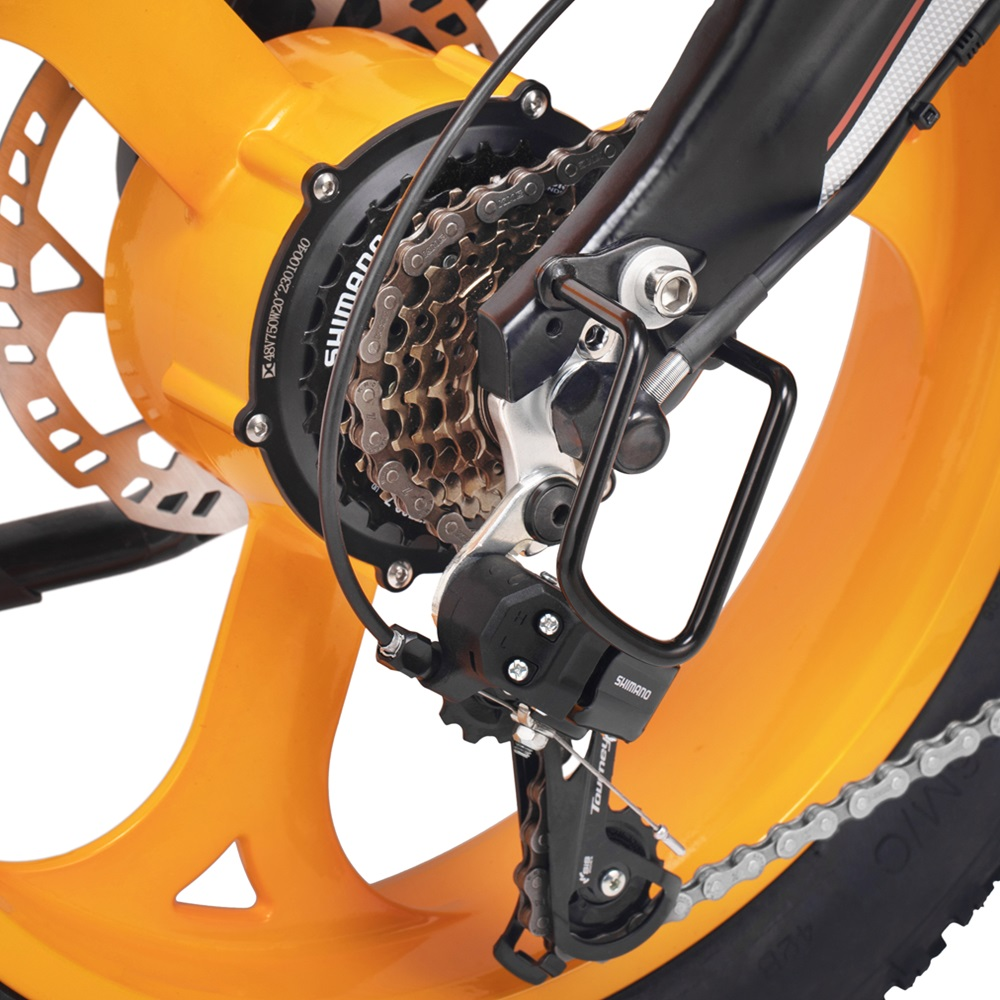 Nahaufnahme eines orangenen Fahrradrads mit schwarzem Schaltwerk und Kette, Shimano-Komponenten sichtbar.