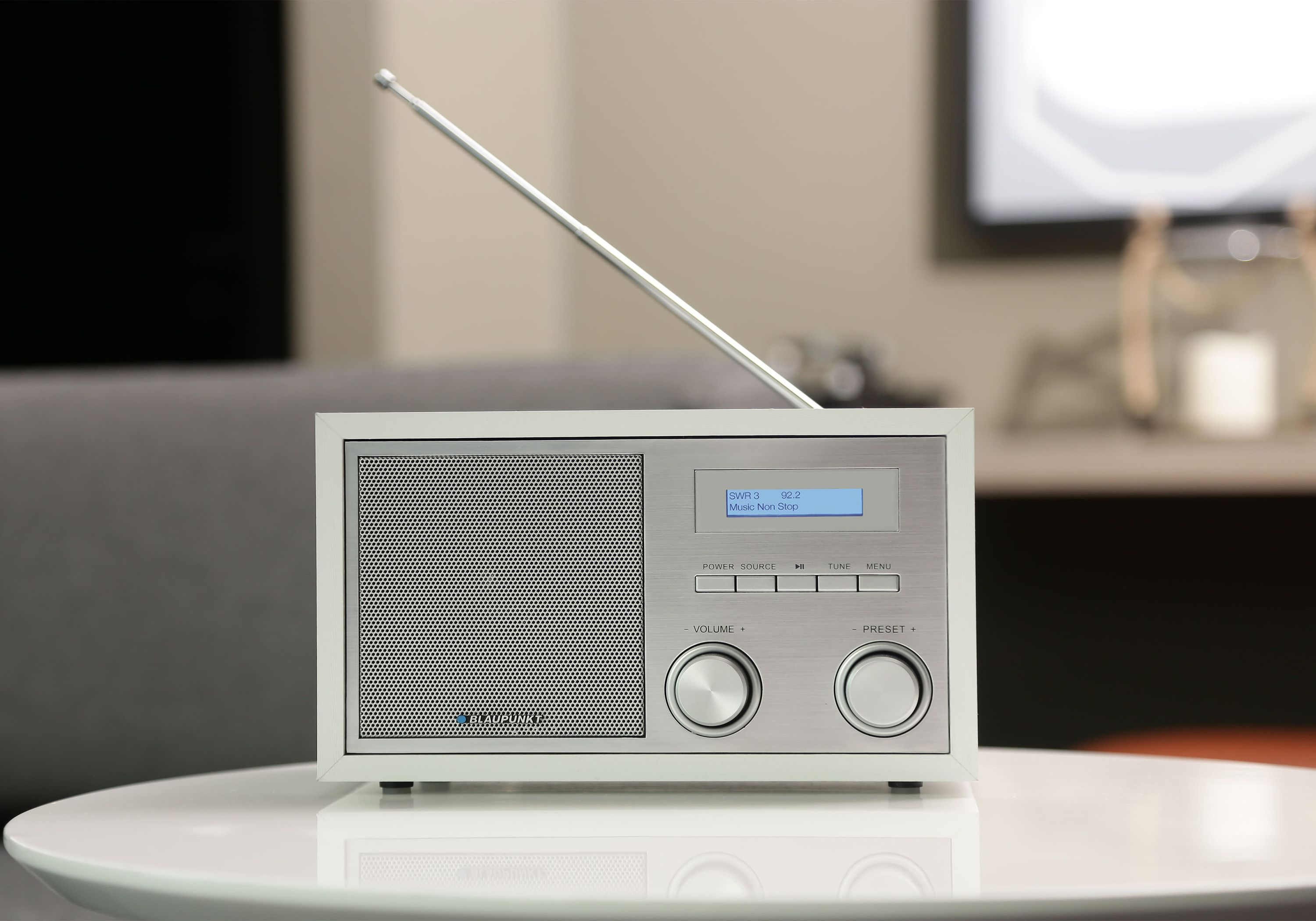 Weißes Radio auf einem weißen Tisch, in einem Wohnzimmer. Mit silberner Antenne und Knöpfen.
