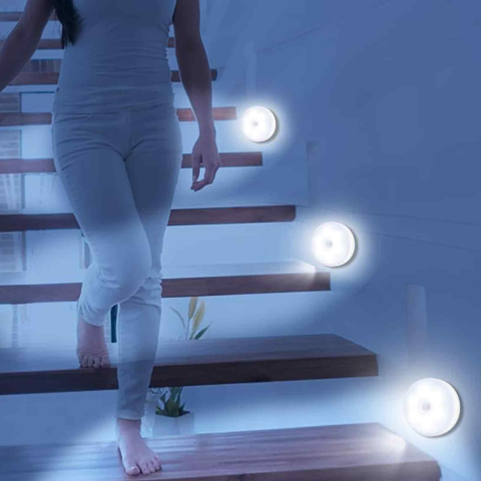 Eine Person geht eine Treppe hinunter, wobei drei Lichter den Weg beleuchten. Die Szene spielt nachts.