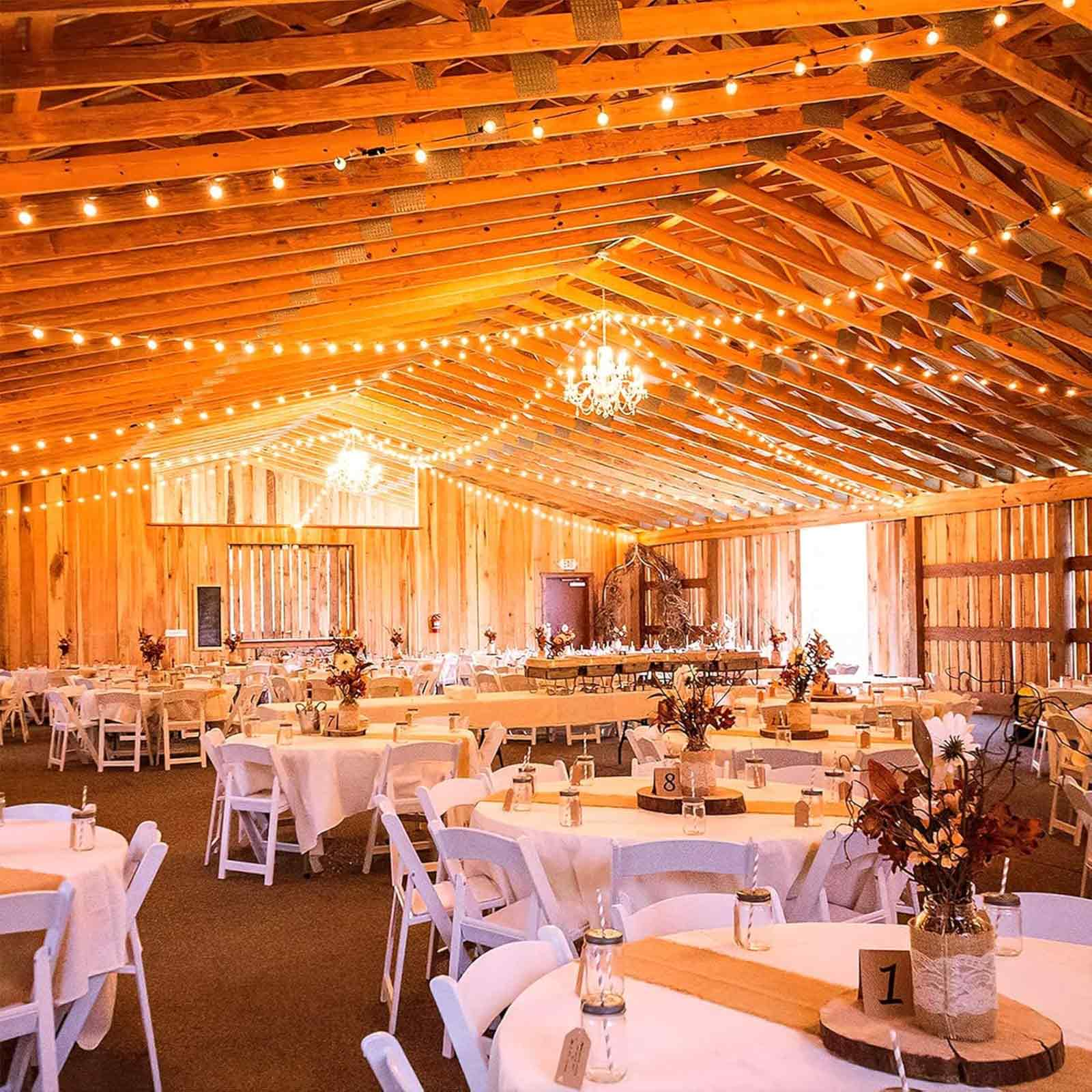 Innenraum einer Scheune aus Holz, Tische für eine Hochzeit, Lichterketten und Dekorationen.
