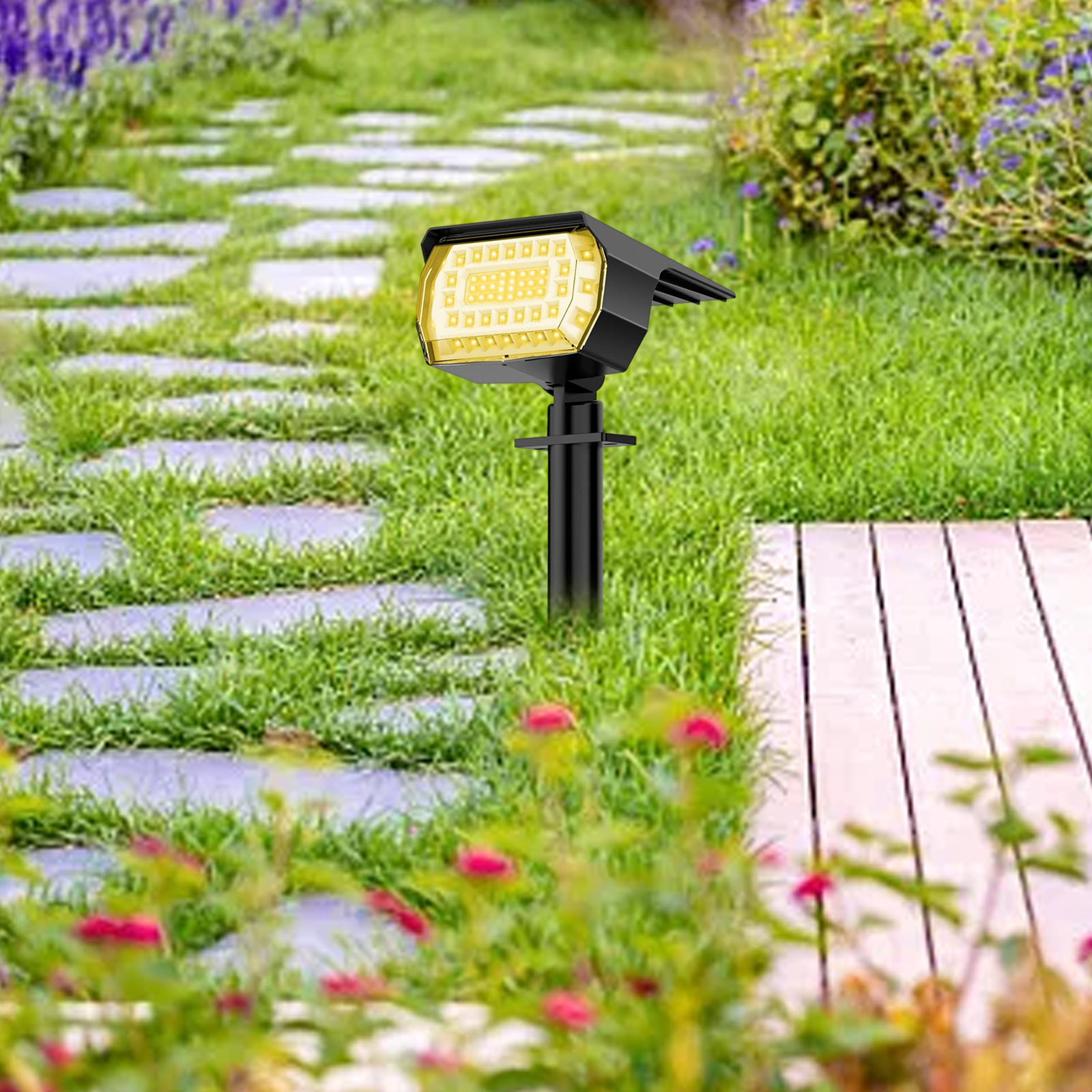Solarbetriebener Strahler, der einen Weg in einem Garten mit roten Blumen beleuchtet.