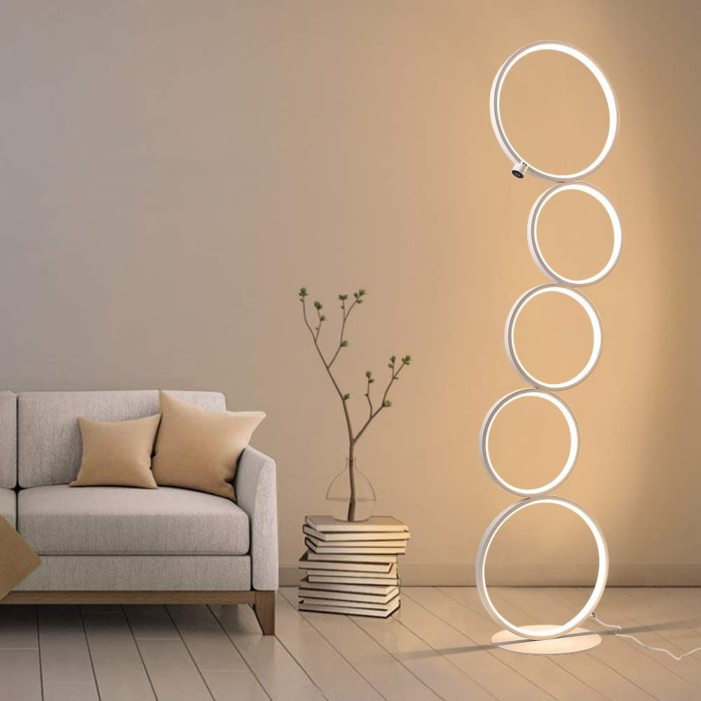 Eine hohe, weiße Stehlampe mit fünf kreisförmigen Lichtquellen. Eine Vase mit einer Pflanze und ein Bücherstapel.