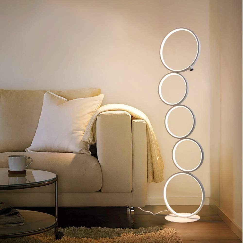 Eine moderne Stehlampe mit kreisförmigen Lichtern, im Hintergrund ein Sofa und ein Tisch. Warmes Lichtambiente.
