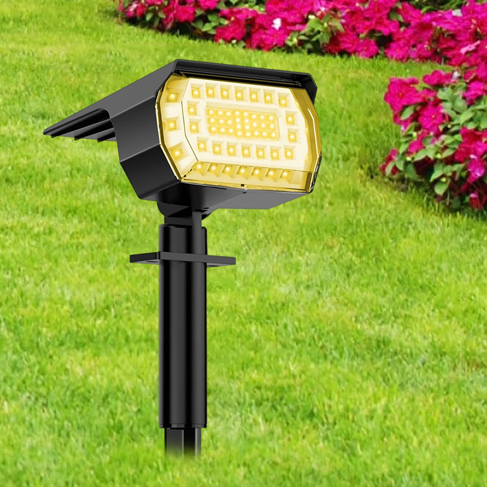 Schwarzer Solar-Spot im Garten. Gelbe Lichter auf dem Panel, mit Gras und Blumen.