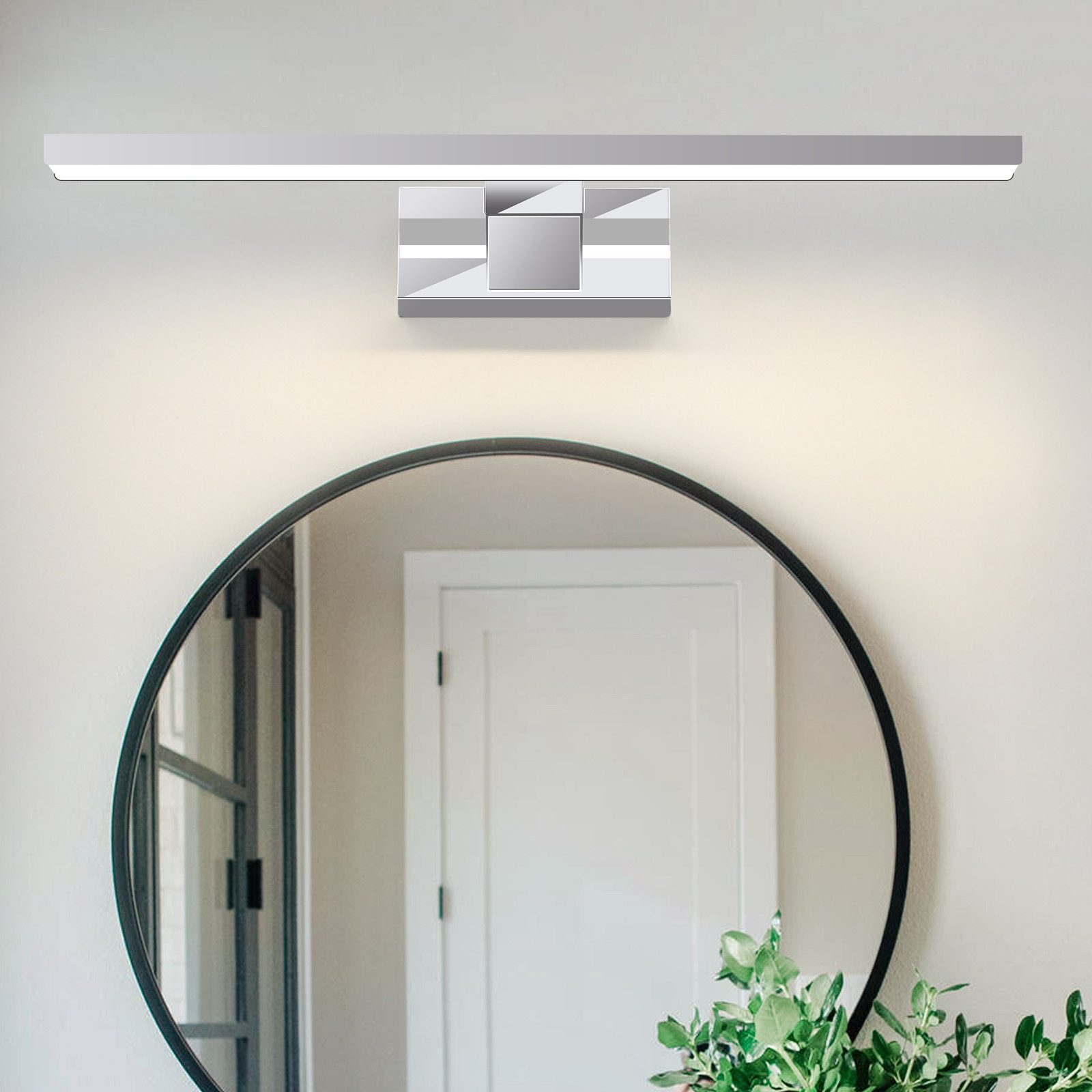 Un apparecchio di illuminazione a LED argentato sopra uno specchio rotondo. Una pianta è alla base.