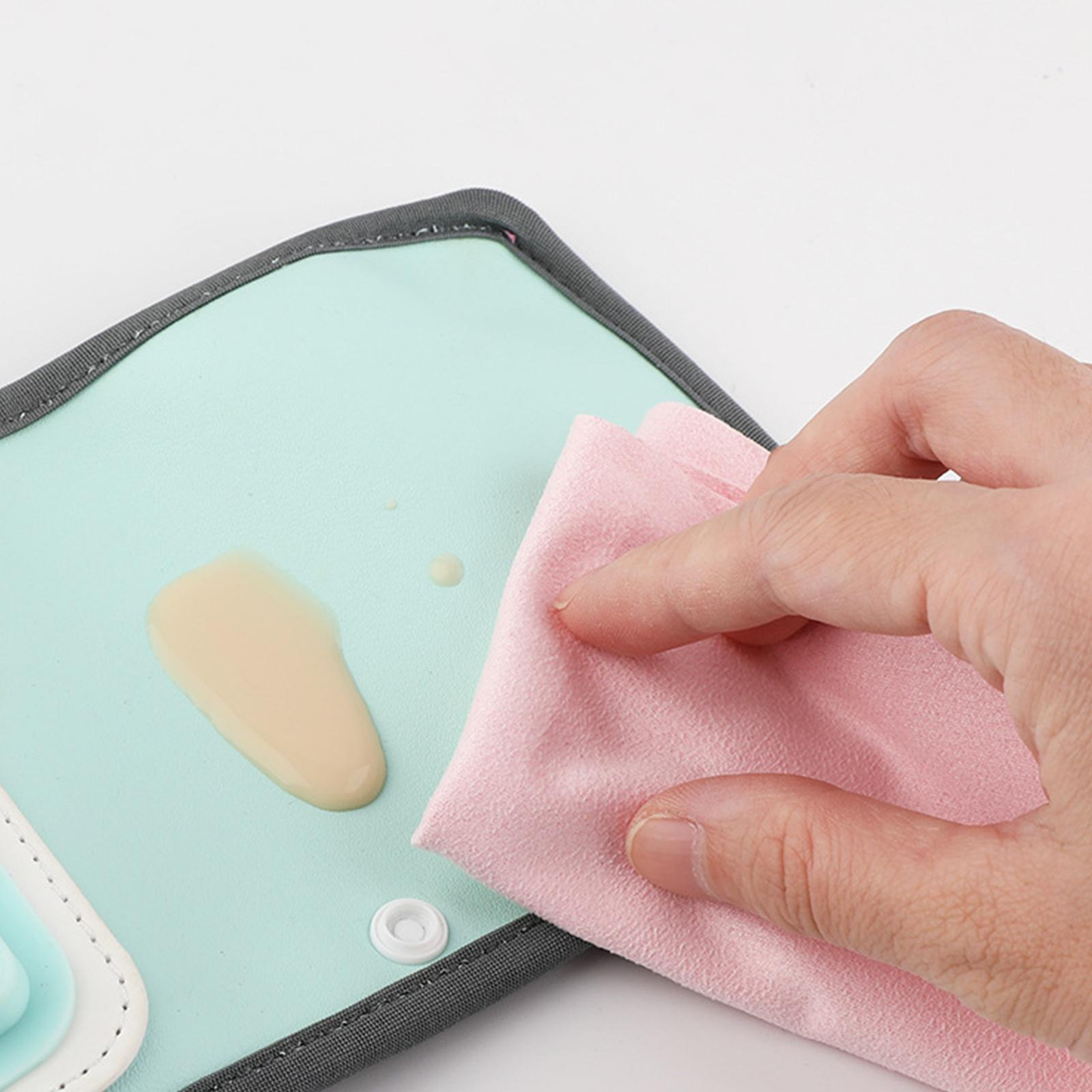 Hand wischt verschüttete Flüssigkeit auf einer türkisfarbenen Oberfläche mit einem rosa Tuch ab. Weißer Hintergrund.