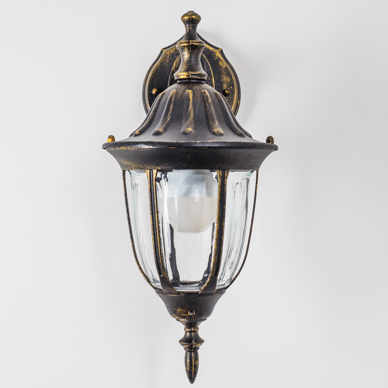 Bronze-Wandlampe mit klarer Glasabdeckung, an einer weißen Wand montiert. Klassisches Design.