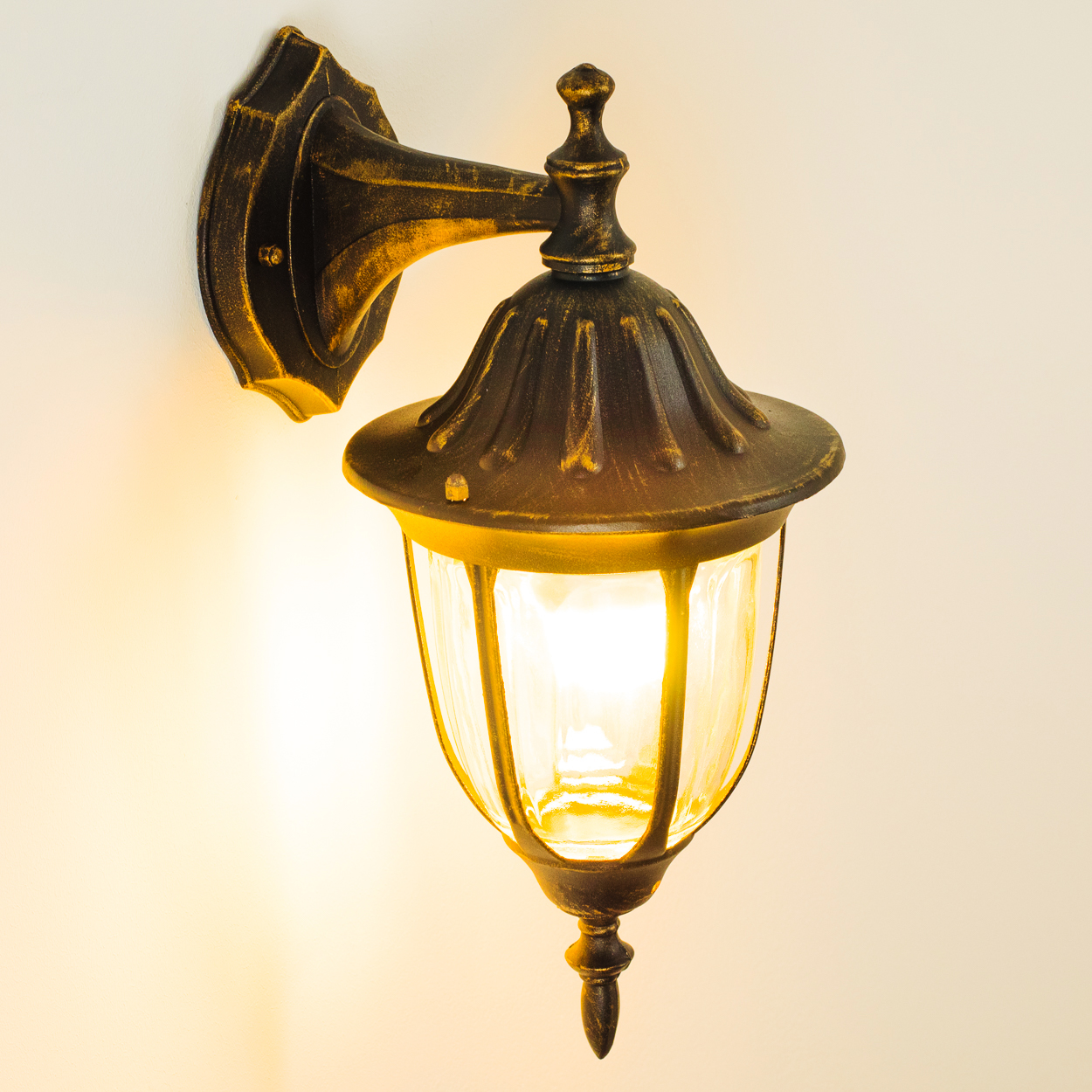 Bronze Wandlampe mit klarem Glasschirm, eingeschaltet, wirft Licht auf die Wand.