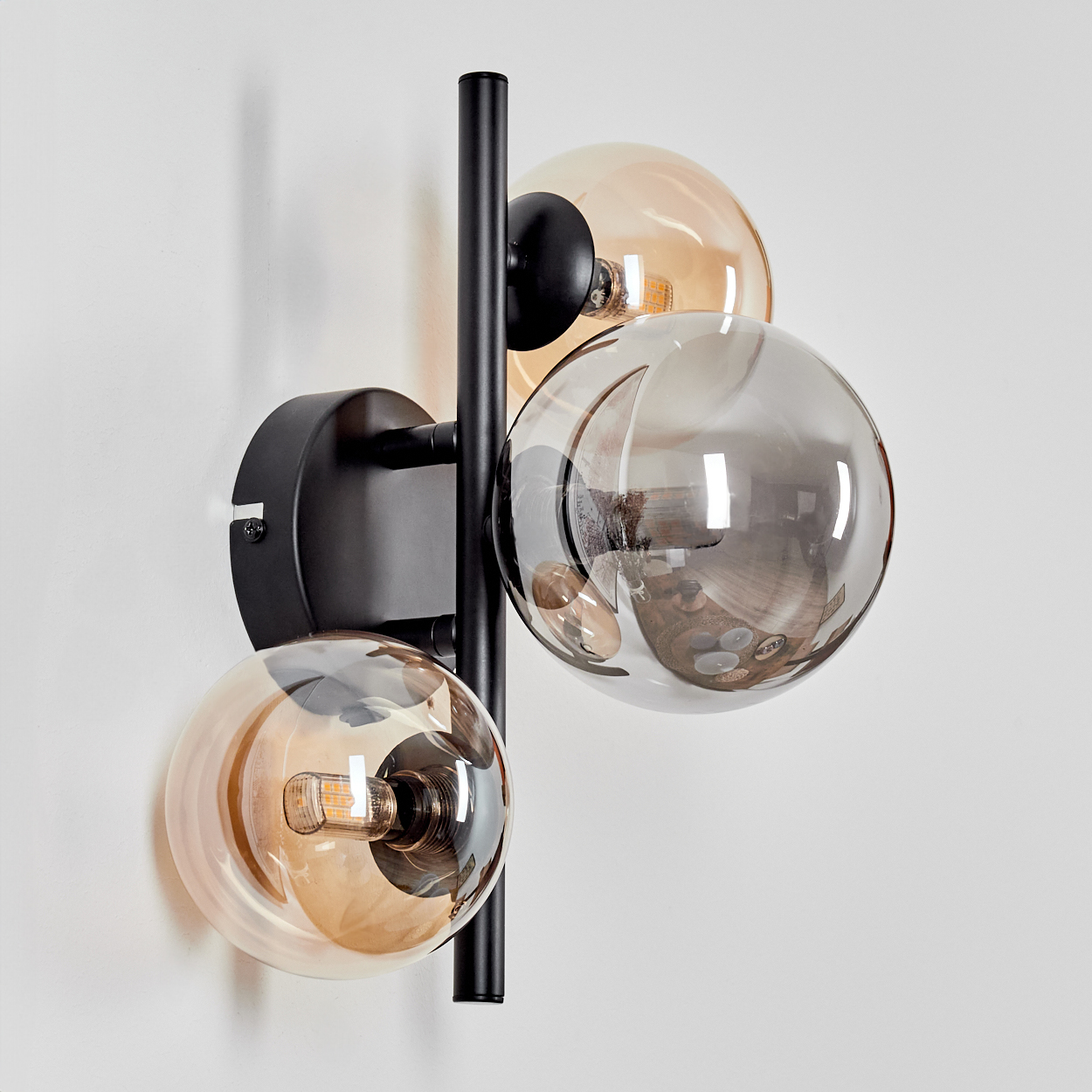 Wandlampe mit drei Glaskugeln, bernsteinfarben und grau, auf schwarzem Rahmen, vor weißem Hintergrund.