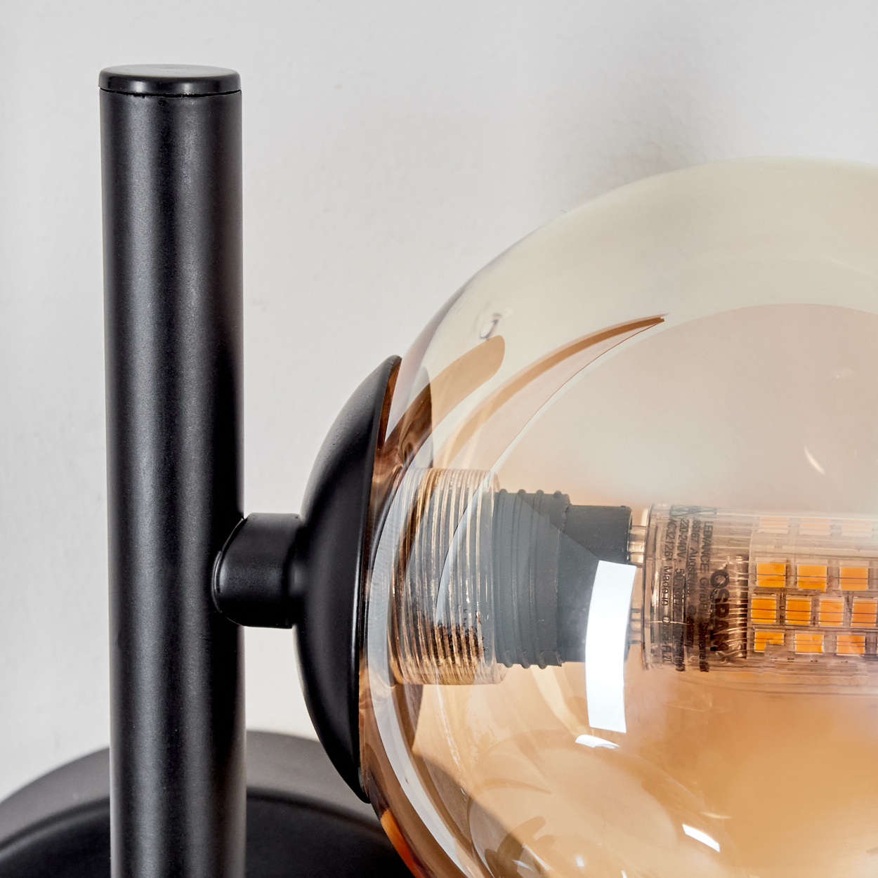 Nahaufnahme einer Wandlampe mit einer gerippten Glaskugel, bernsteinfarben, und einem schwarzen Rahmen.