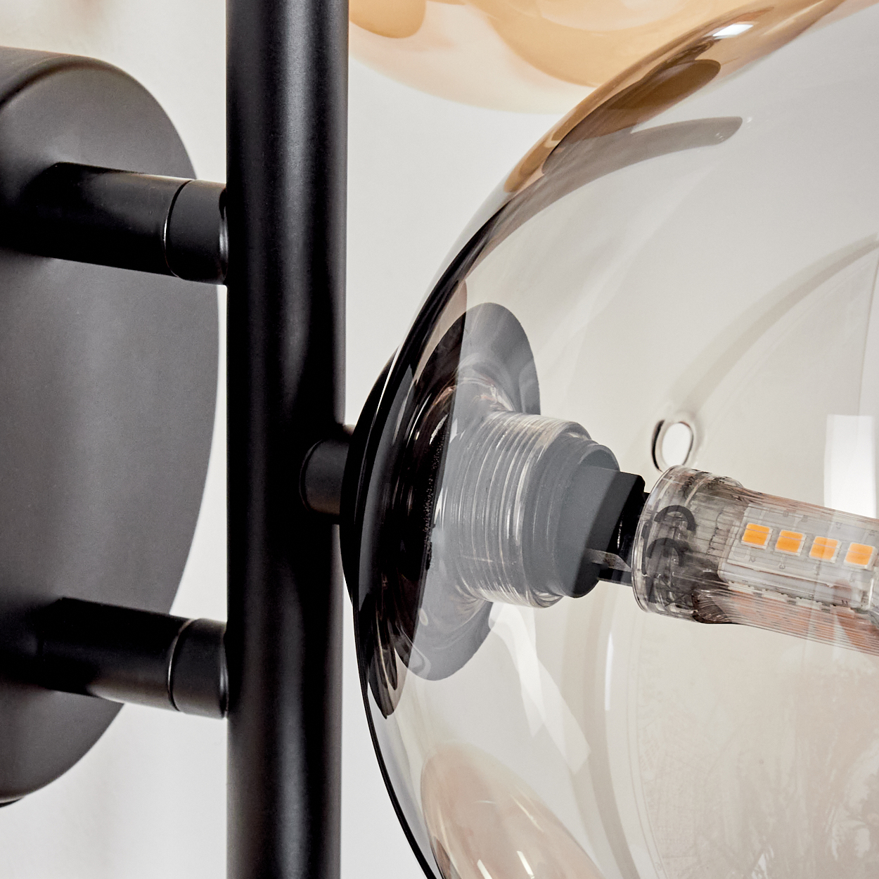 Nahaufnahme einer transparenten Glaskugel mit sichtbarer LED-Glühbirne. Die Glühbirne emittiert ein warmes, oranges Licht.