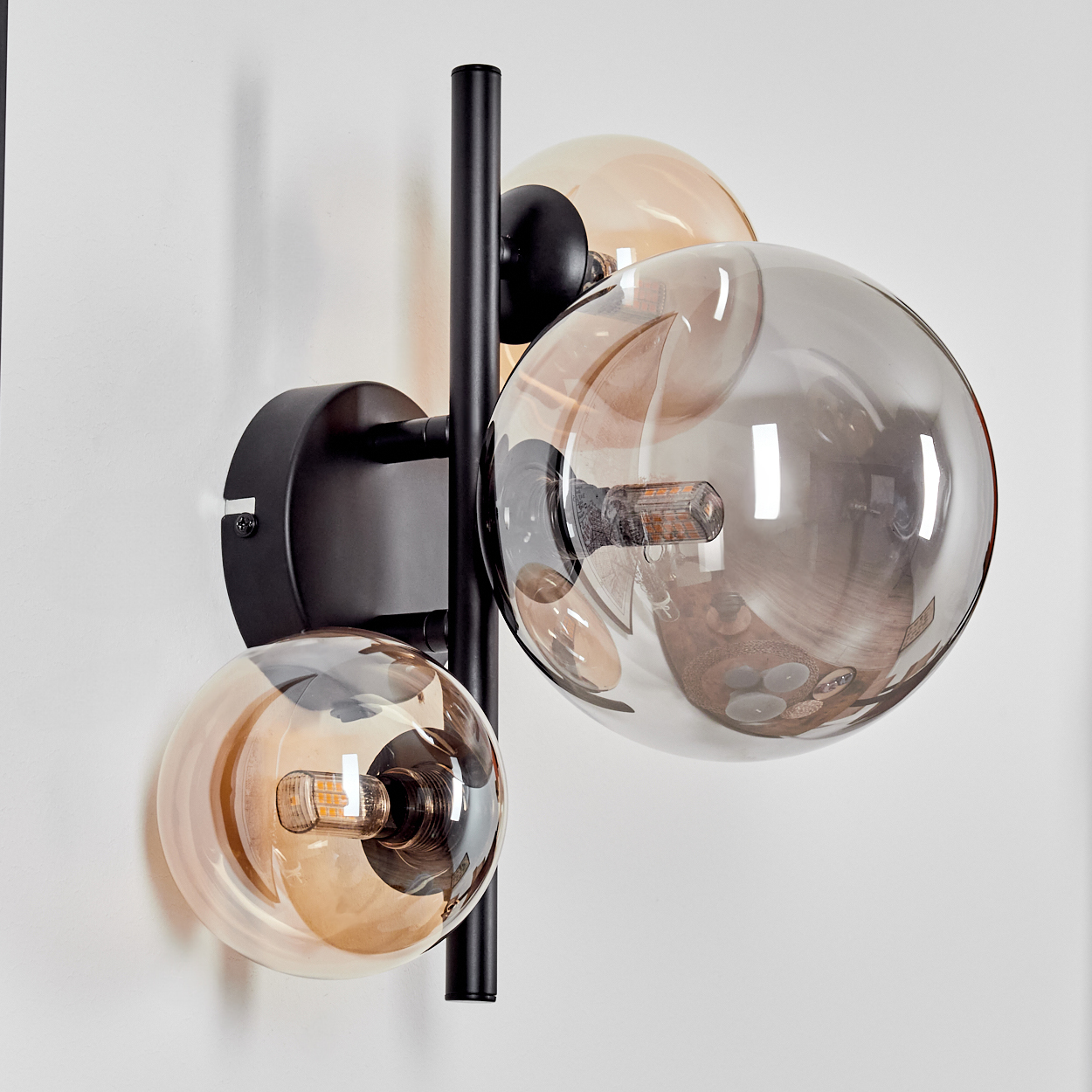 Eine Wandlampe mit drei braunen Glaskugeln. Die Lampen sind eingeschaltet.
