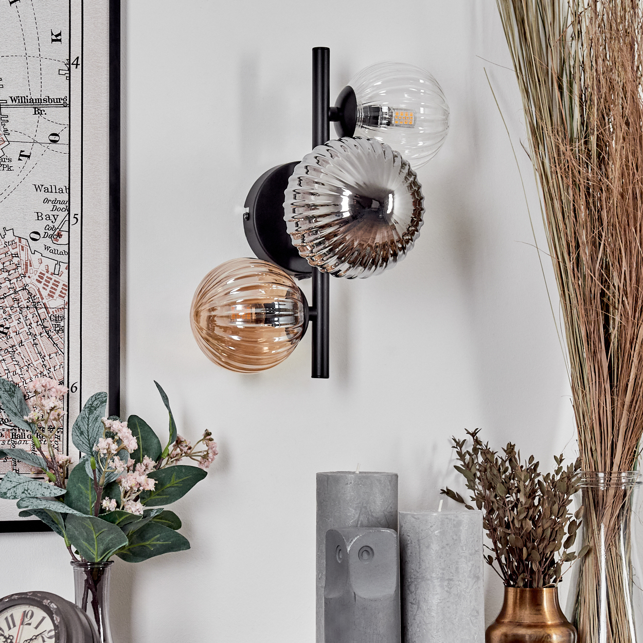 Eine Wandlampe mit drei Schirmen, zwei silbernen und einem bernsteinfarbenen, vor einem Hintergrund von Heimdekoration.