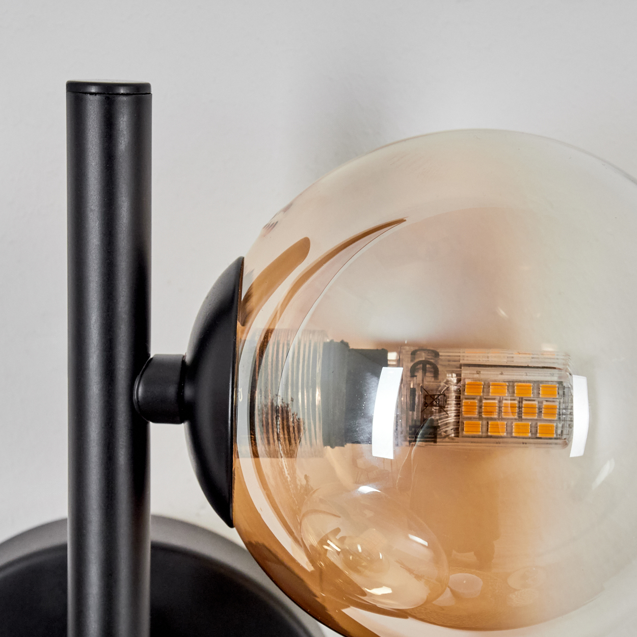 Schwarze Lampe mit bernsteinfarbener Glaskugel. Nahaufnahme der Lampe vor weißem Hintergrund.