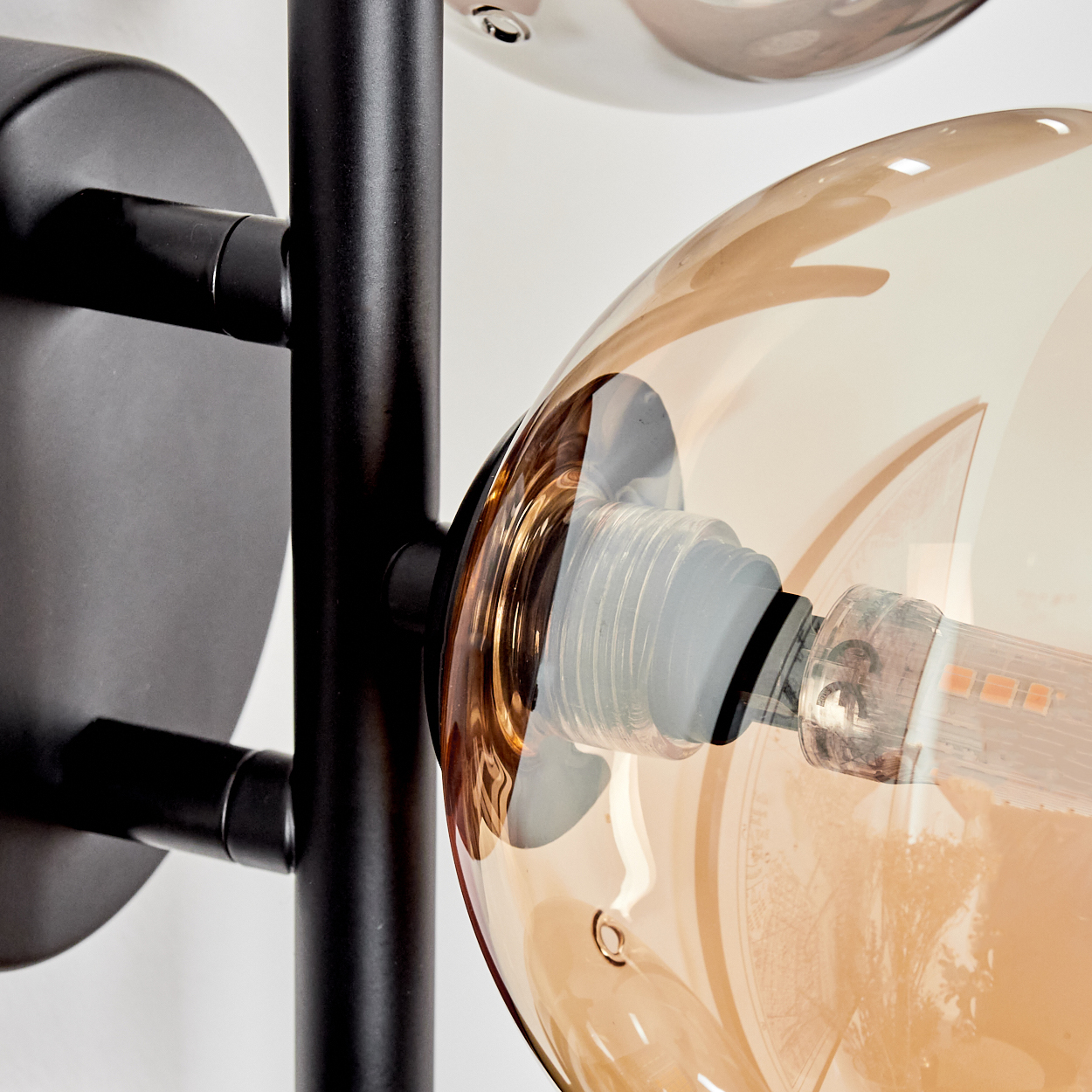Nahaufnahme einer Glühbirne in einer bernsteinfarbenen Glaskugel, Teil einer Wandlampe.