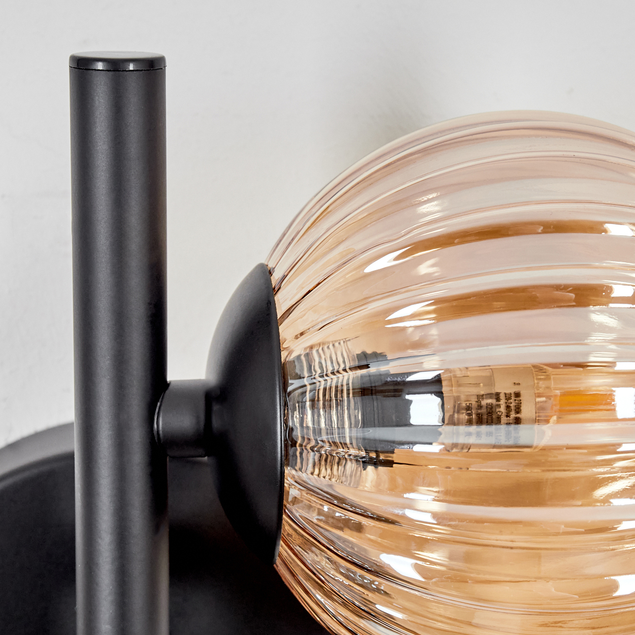Nahaufnahme einer Wandlampe mit gerippter, bernsteinfarbener Glaskugel. Schwarzer Metallarm und -befestigung.
