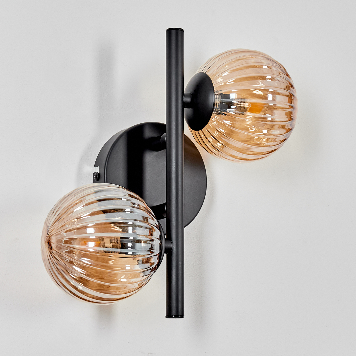 Wandlampe mit zwei bernsteinfarbenen Glaskugeln. Die Lampe ist schwarz, mit vertikalem Metallträger.