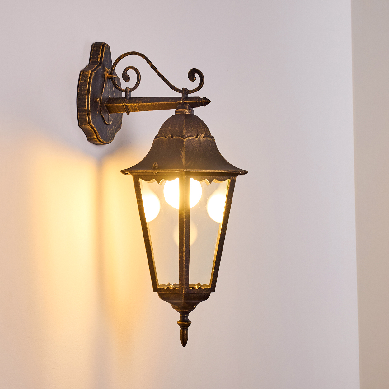 Verzierte Wandleuchte mit schwarz-goldener Oberfläche, an einer weißen Wand.