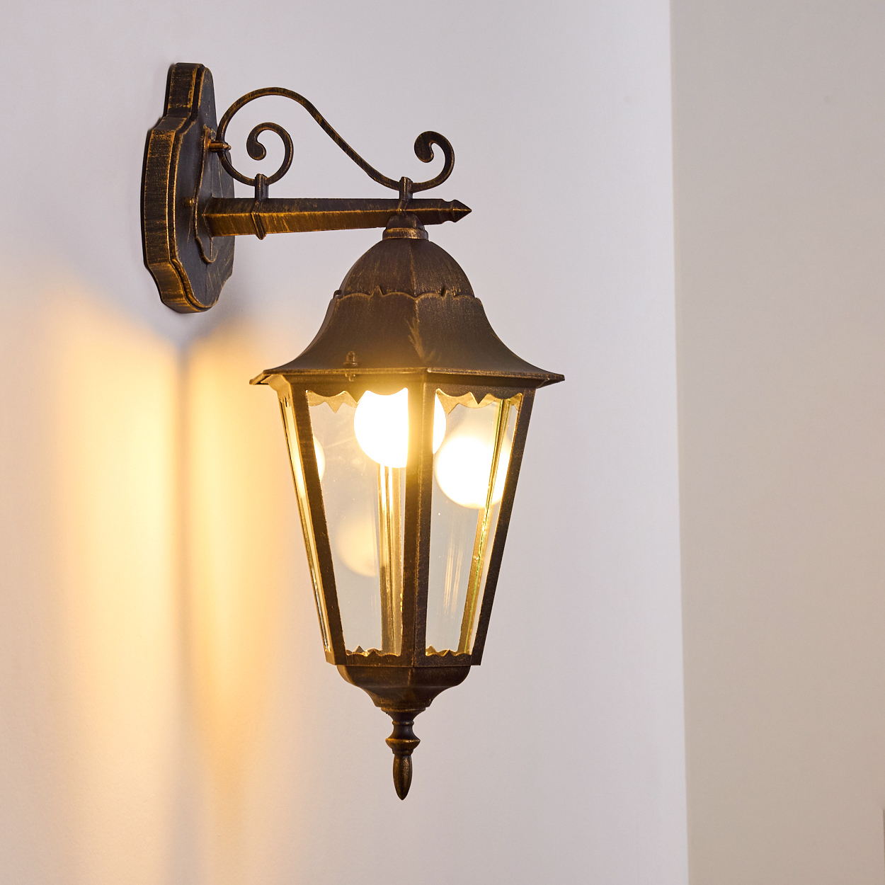Verzierte Wandleuchte mit schwarz-goldener Oberfläche, an einer weißen Wand.