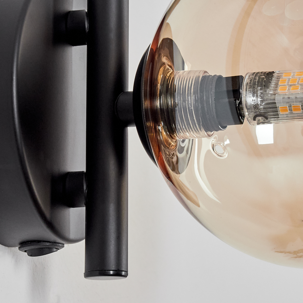 Nahaufnahme einer schwarzen Wandlampe mit bernsteinfarbener Glaskugel und sichtbarer Glühbirne.