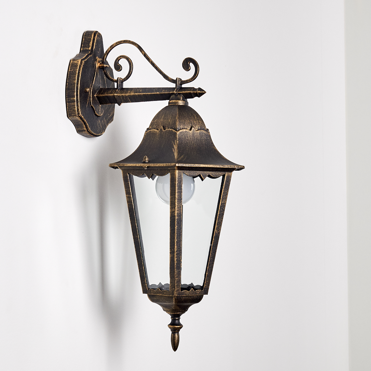Eine antike Wandleuchte mit schwarz-goldener Oberfläche an einer weißen Wand. Sie hat einen klaren Glasschirm.