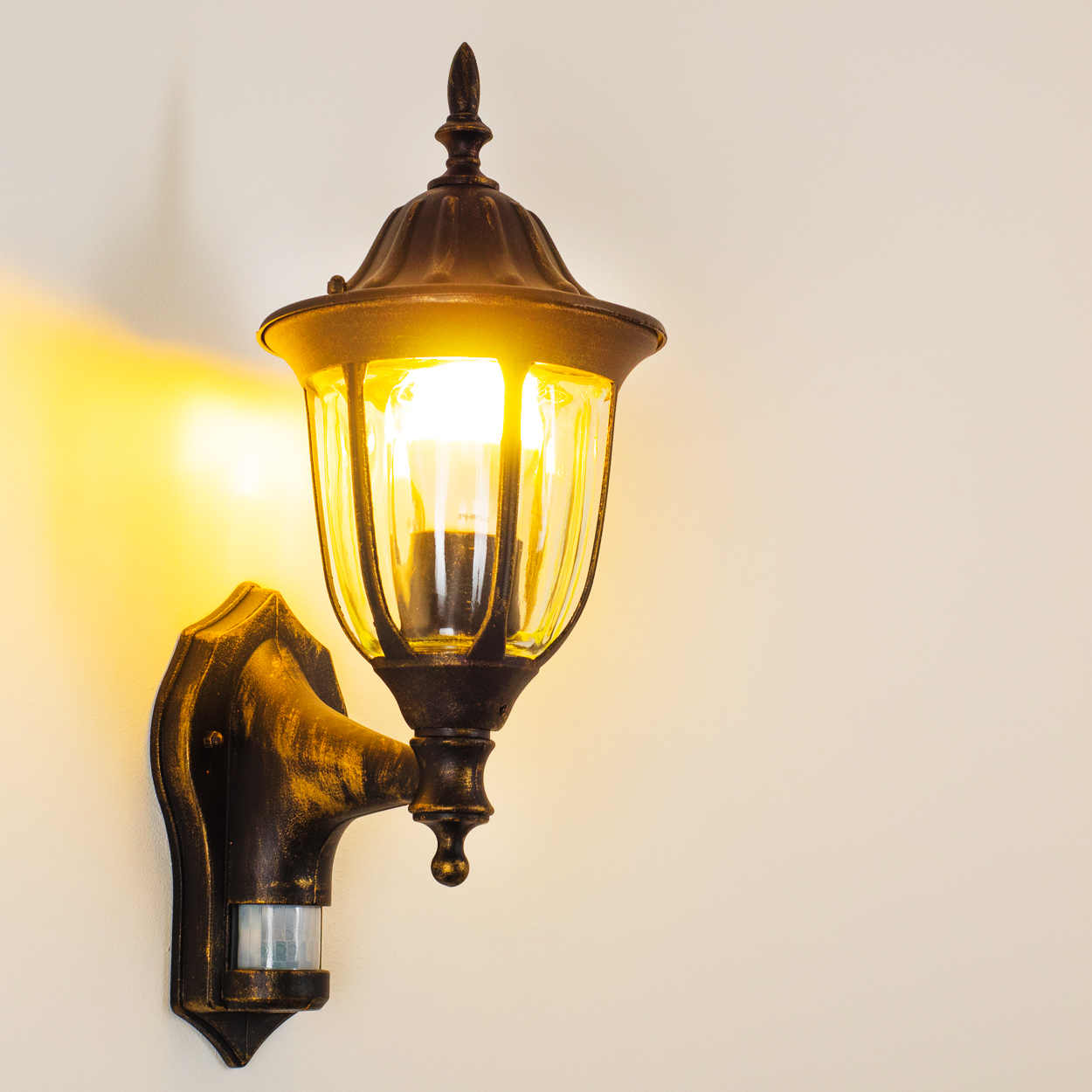 Bronze-Außenwandleuchte mit warmem Licht, das die Wand beleuchtet.