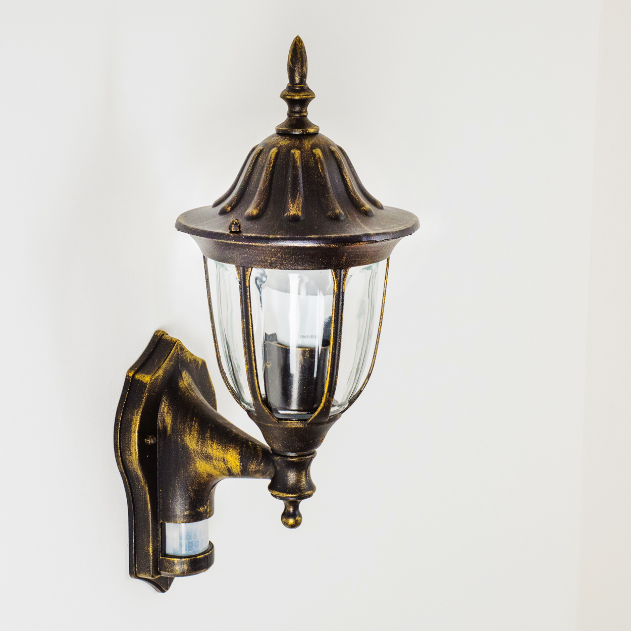 Verzierte Bronze-Wandlampe an weißer Wand. Klarglasschirm.