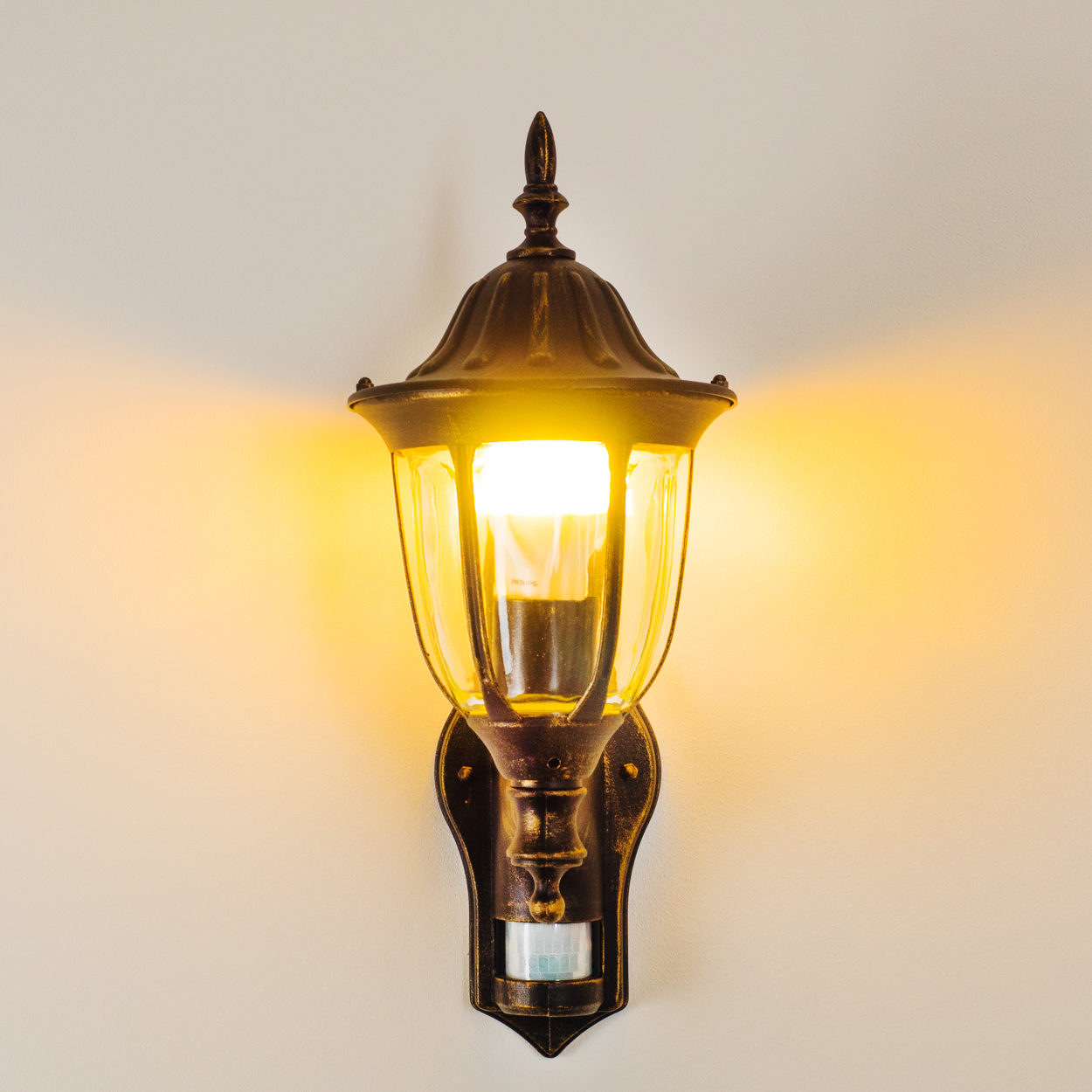 Eine goldene Wandleuchte. Das Licht scheint hell und beleuchtet die Umgebung.
