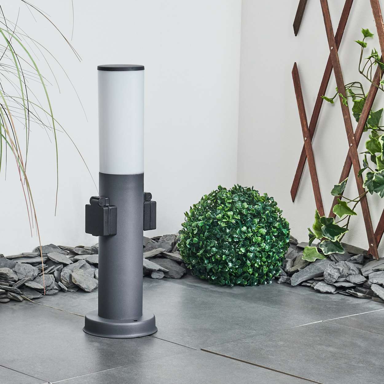 Außenlampe mit grauem Sockel und weißem Oberteil, in einer Gartenszene.
