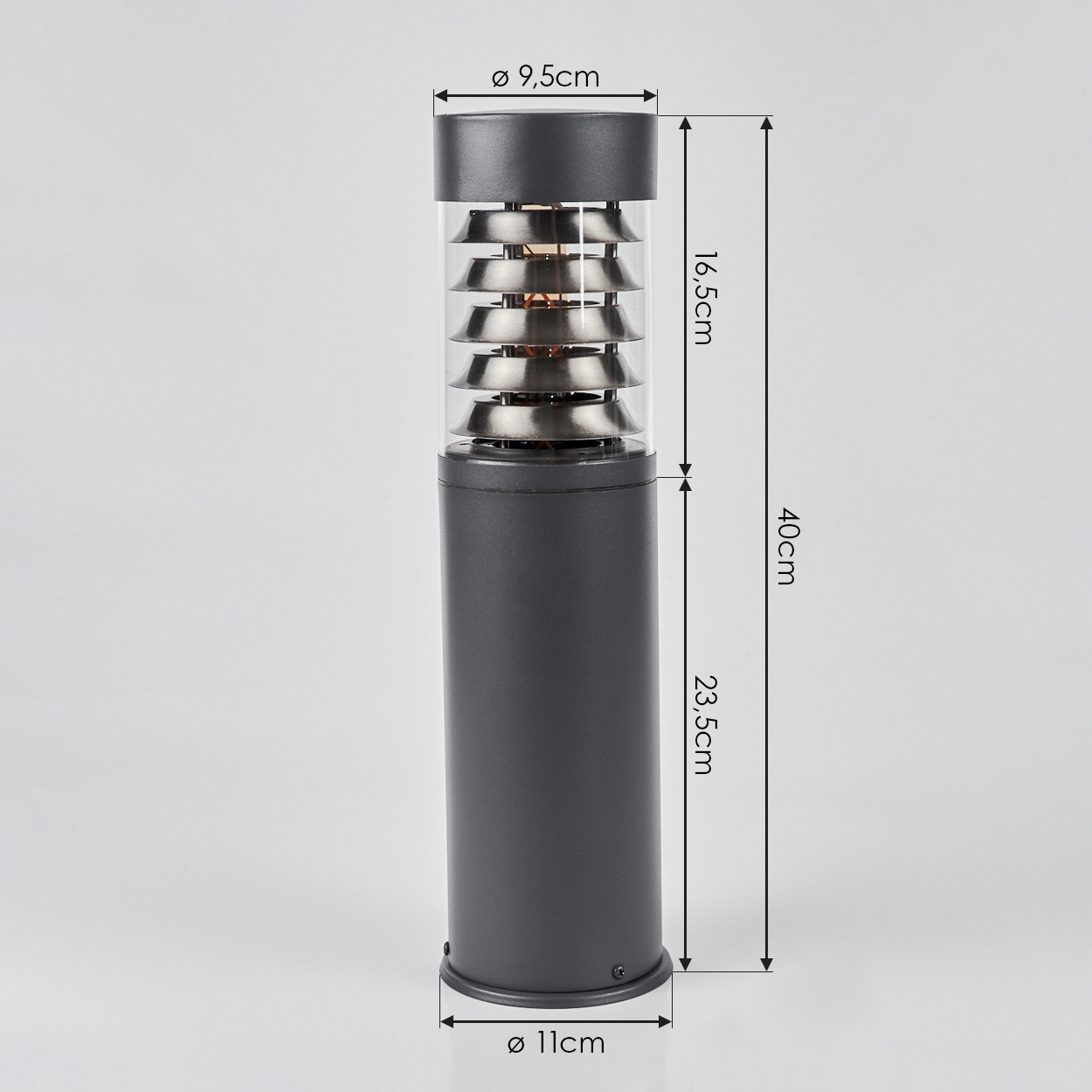Dunkelgraue Außenlampe, zylindrisch, mit horizontalen Metalllamellen in klarem Glas, auf weißem Hintergrund.