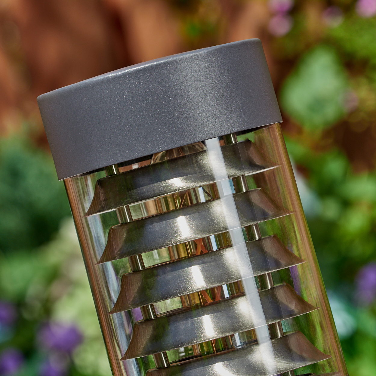 Nahaufnahme der Metalllamellen einer dunkelgrauen Außenlampe in einem klaren Glaszylinder.