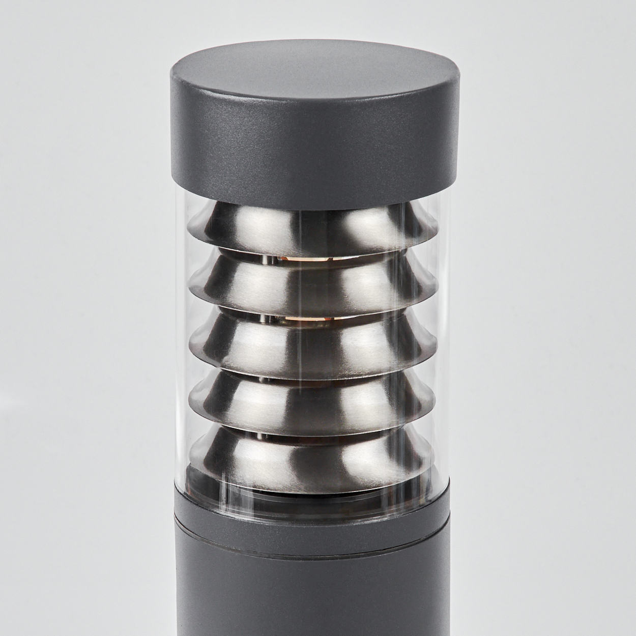 Nahaufnahme der Metalllamellen einer dunkelgrauen Außenlampe in einem klaren Glaszylinder.