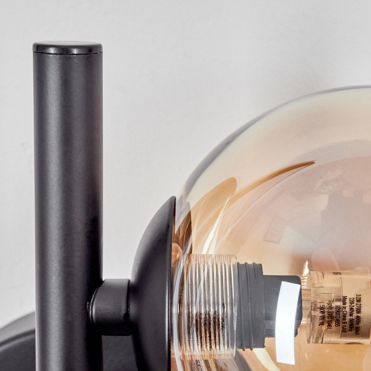 Nahaufnahme einer schwarzen Wandleuchte mit einem kugelförmigen Schirm aus bernsteinfarbenem Glas. Der Hintergrund ist eine weiße Wand.