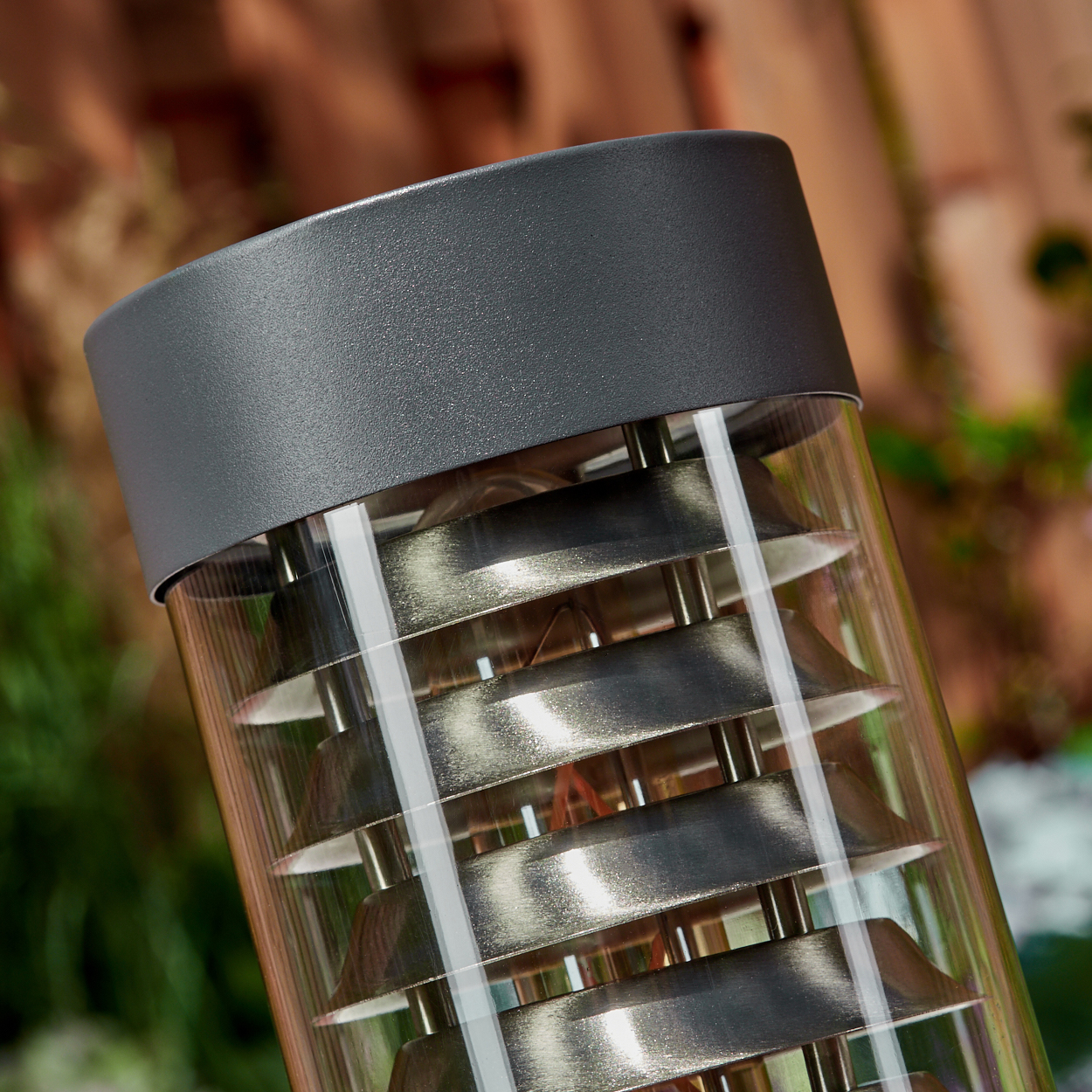 Nahaufnahme einer Außenlampe mit Metallplatten in einem Glasrohr, mit unscharfem Hintergrund.