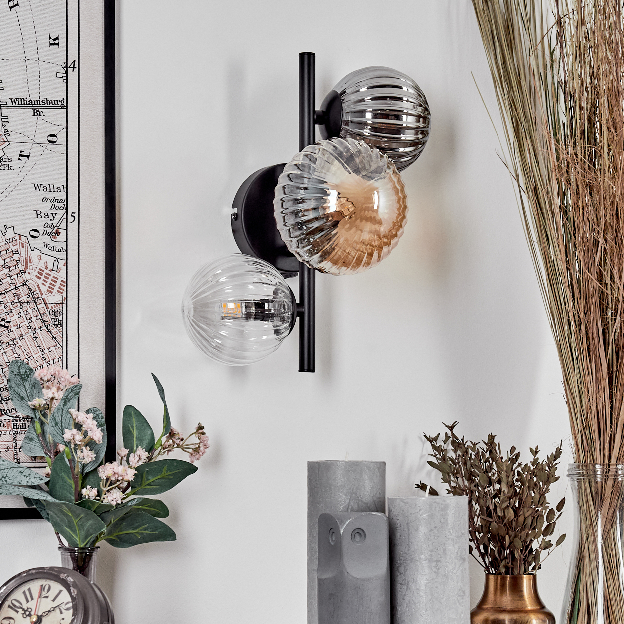 Wandlampe mit drei Glaskugeln, zwei klaren und einer bernsteinfarbenen, auf schwarzem Metallrahmen.