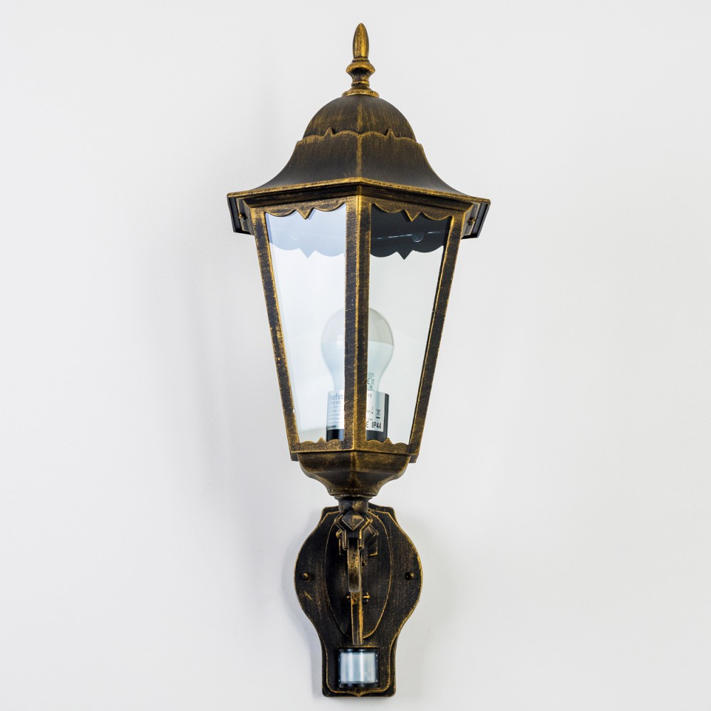 Eine goldene Wandlampe mit Glasfront, montiert an einer weißen Wand. Sie hat einen Bewegungssensor.